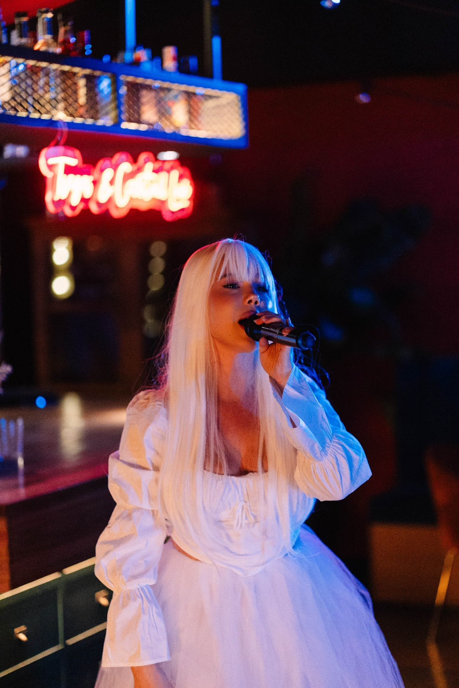 Rocío Hernández cantando con vestido blanco bajo un neón rojo
